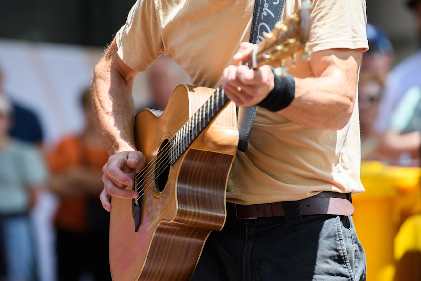 a close-up photo of a man playing an acoustic guitar, his head is cropped out of the frame