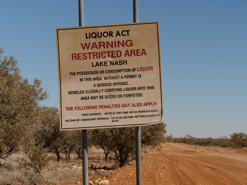 A sign on the side of dusty dirt road reads 'liquor act: warning restricted area'.