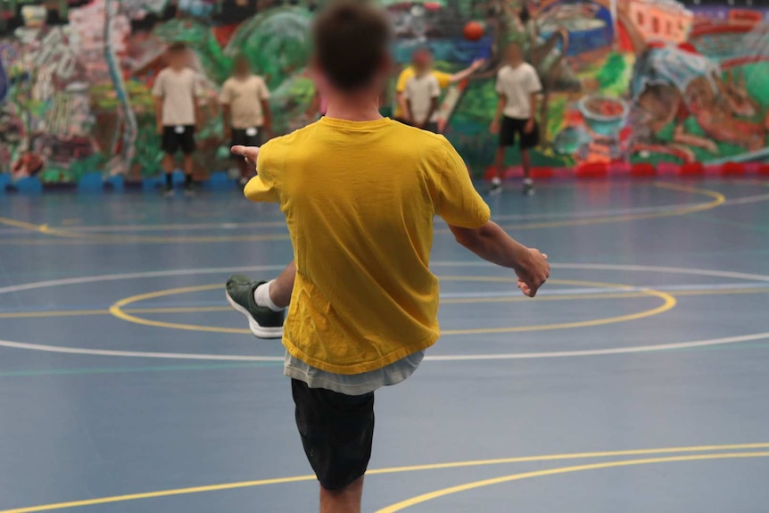 A group of teenage boys wait for another teen in the foreground to kick a football. All faces are blurred