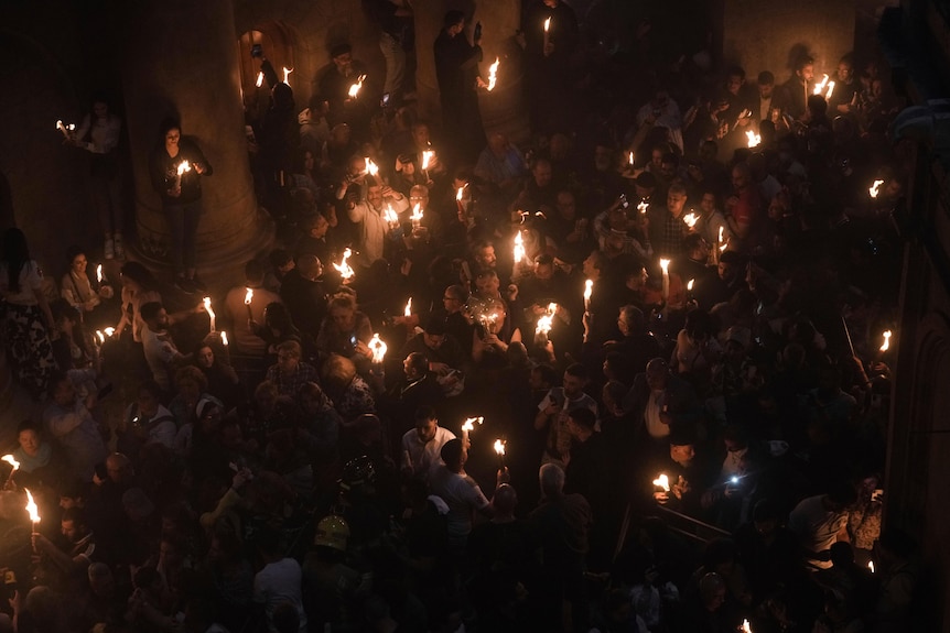 People gathered together, with some holding large candles with are alight.