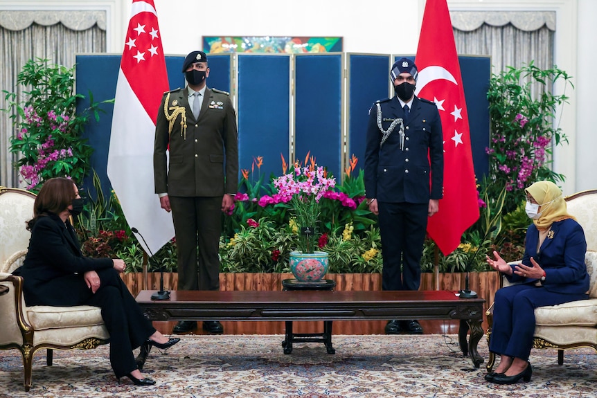   Kamala Harris i prezydent Singapuru Halima Yacoub siedzą naprzeciwko siebie, za strażnikami i flagami Singapuru. 