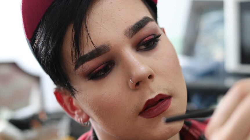 A young man in makeup holding an eyeliner pencil