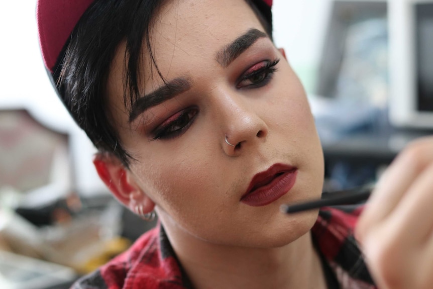A young man in makeup holding an eyeliner pencil