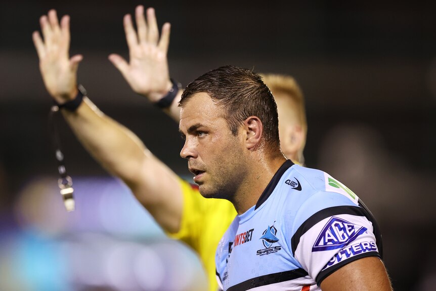 Cronulla Sharks' Wade Graham walks off the NRL field as the referee signals 10 minutes in the sin bin behind him.