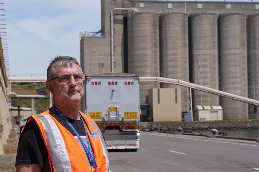 Man left of frame with grain silos and truck in background at a port facility