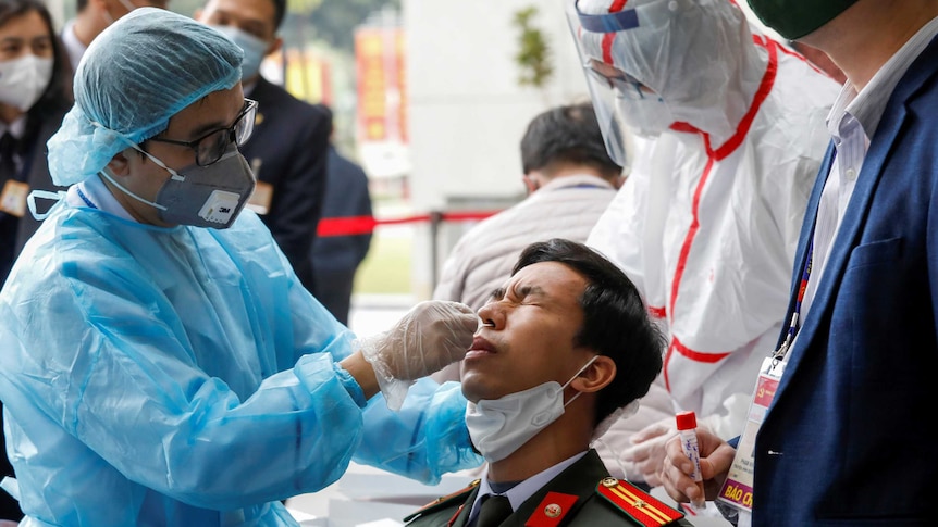 A man in uniform flinches as he receives a nasal swab from a man in protective gear
