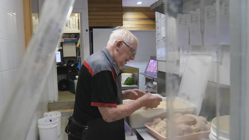 An old man crumbing chicken fillets