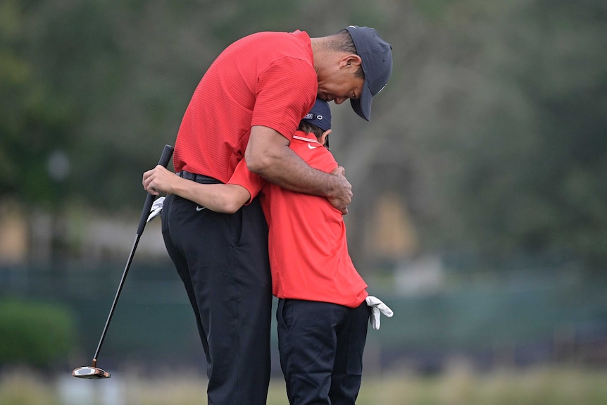 Tiger Woods hugs his son, Charlie, both wearing identical red polo shirts