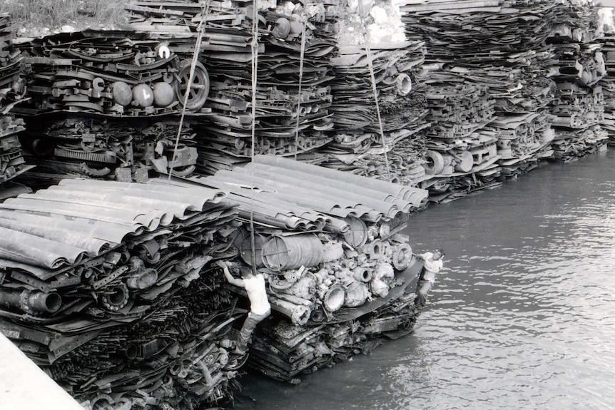 A Japanese worker scales a stack of scrap metal.