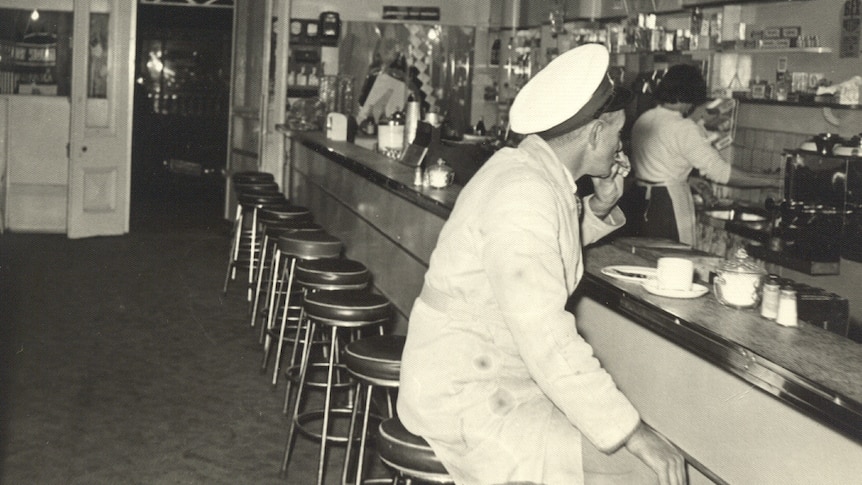 A cafe from 1952, with a milkman sitting at the bench drinking coffee.