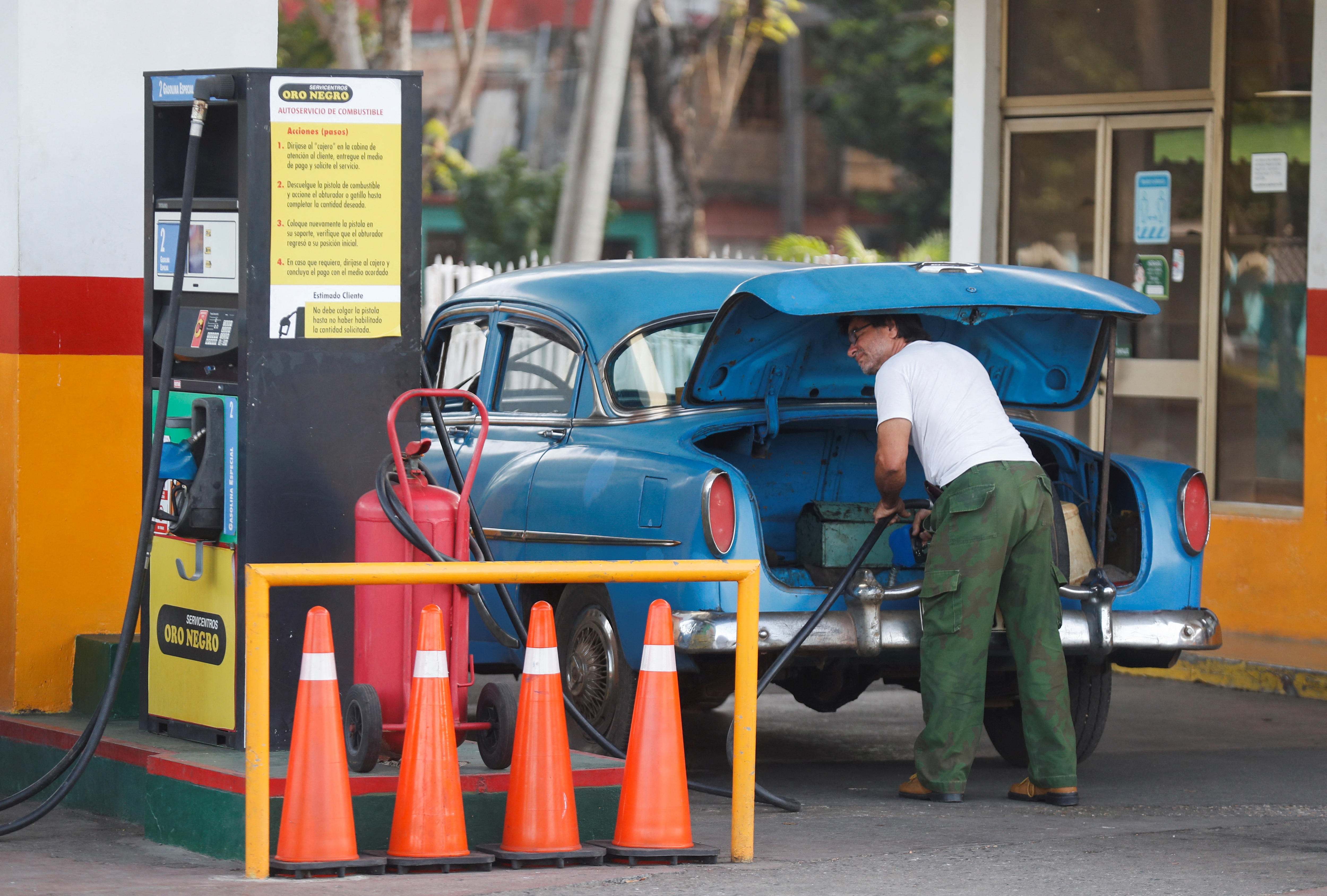 A man fills up a jerry can at a Cuban petrol station in the boot of his blue car