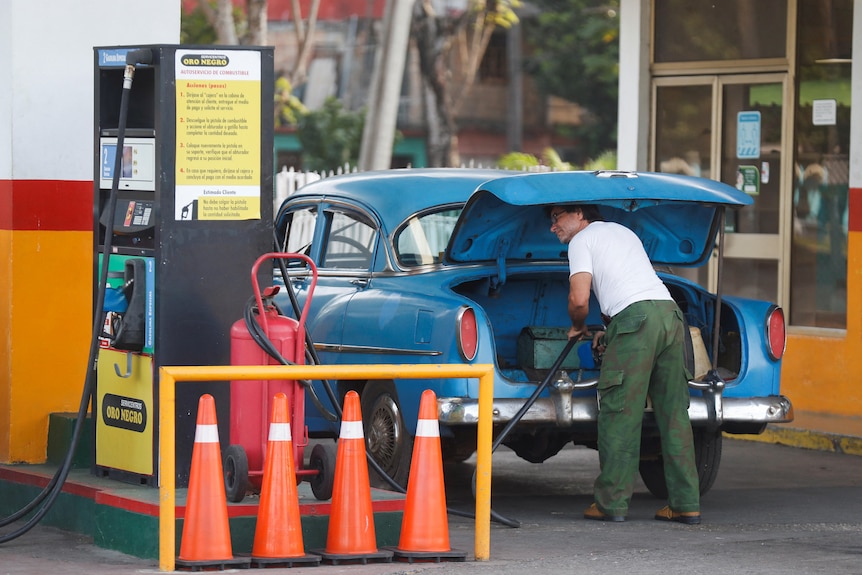 A man fills up a jerry can at a Cuban petrol station in the boot of his blue car