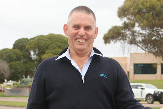 A man in a dark jumper stands outside an office and smile on a cloudy day