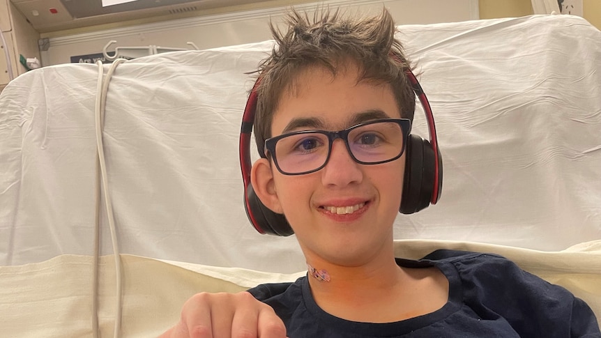 A teenager with headphones on in a hospital bed.