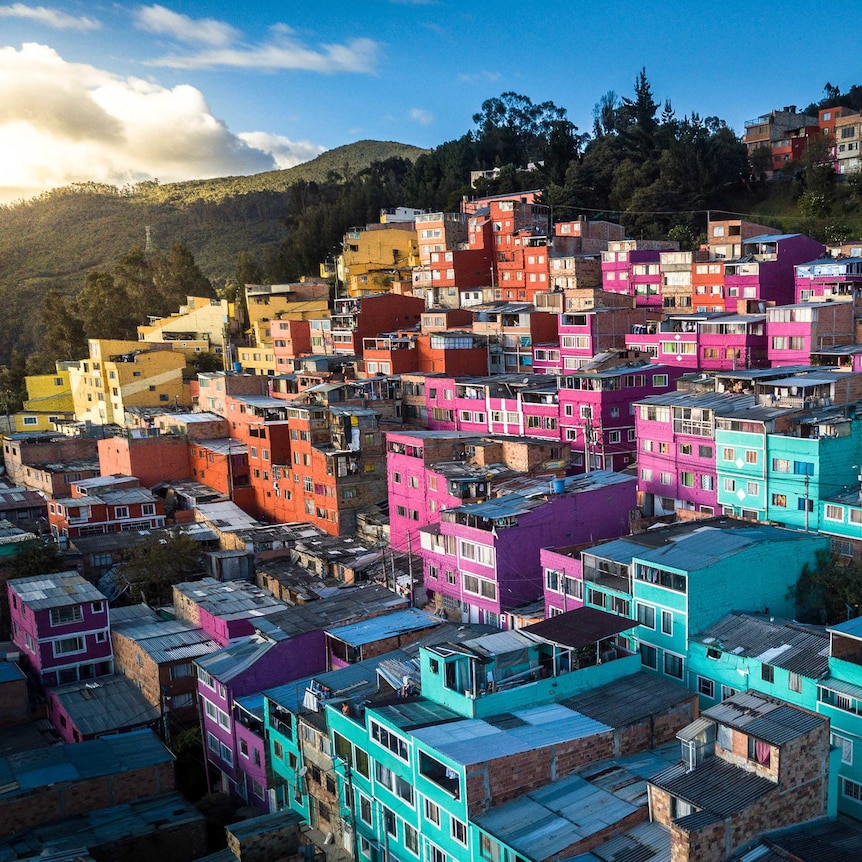 Brightly painted houses build up a hillside and catching the sun. Blue in the foreground moving through purple to yellow.