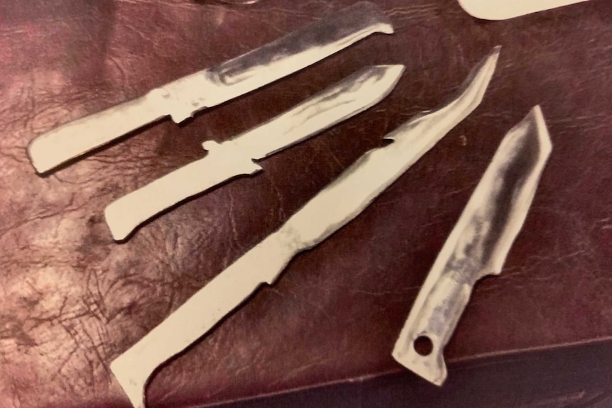 Homemade knives laid out on a surface.