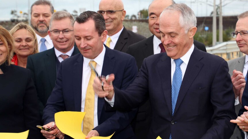 PM Malcolm Turnbull holding scissors, and WA Premier Mark McGowan, cutting a paper ribbon surrounded by MPs.