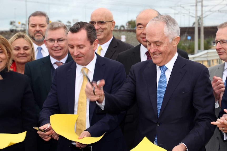 PM Malcolm Turnbull holding scissors, and WA Premier Mark McGowan, cutting a paper ribbon surrounded by MPs.