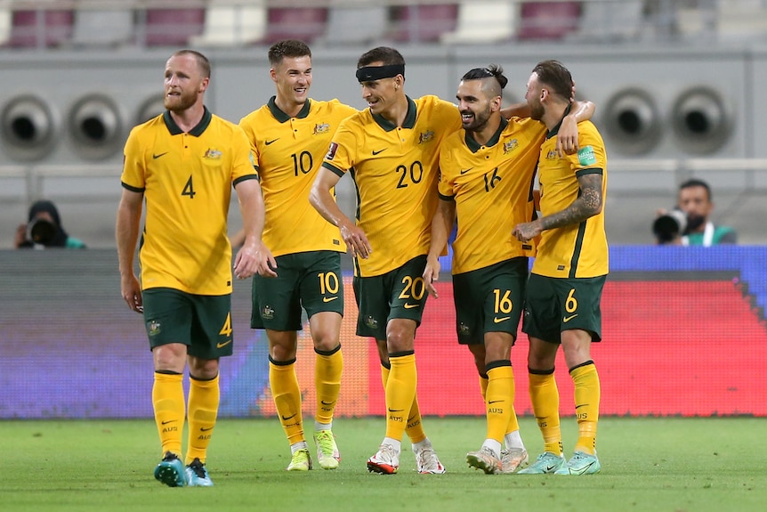 Four Socceroos players smile and stand in a line arm-in-arm, with Rhyan Grant in front of them