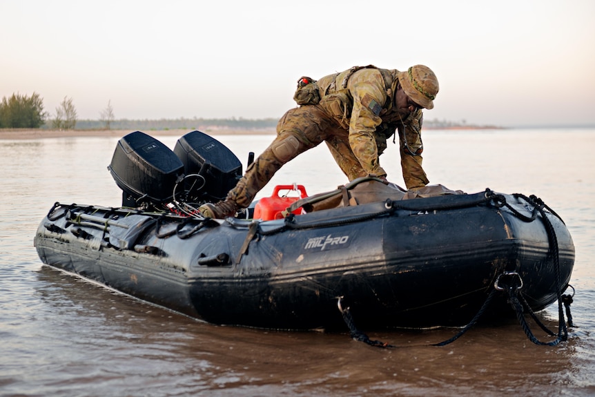 a man in army uniform pushing an inflatable black boat to sea