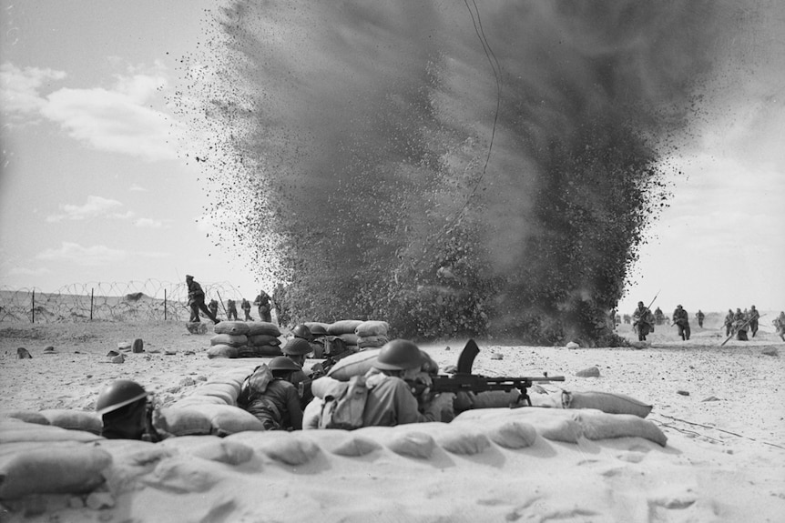 Black and white photo of a machine trench in the foreground and an explosion in the background