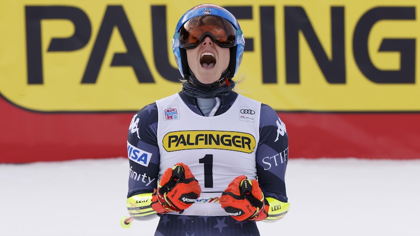 A skiier faces the camera, pumps her fists and roars with her helmet on after winning an event.