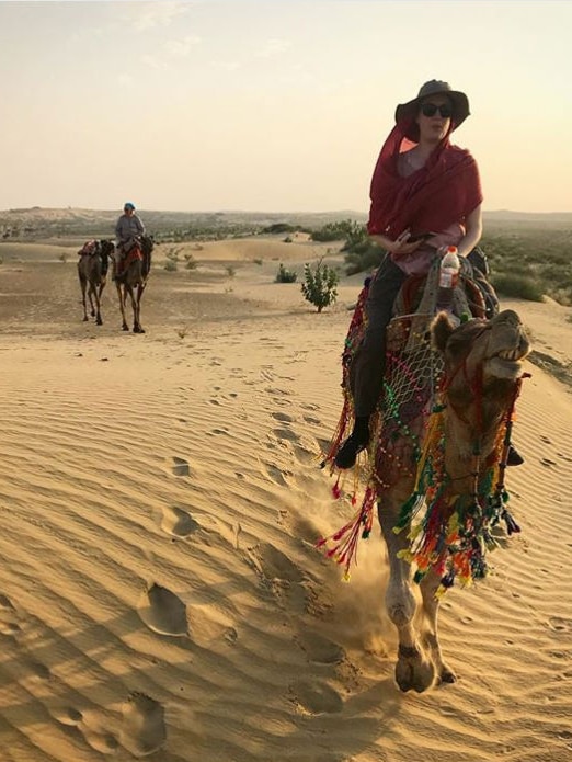 Heanue riding on a camel over desert landscape.