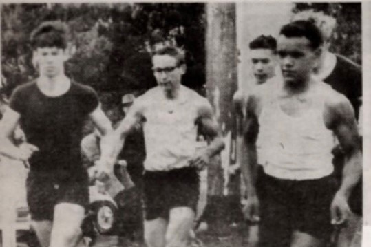 A faded black and white photo of three men crossing the finish line of a running race.