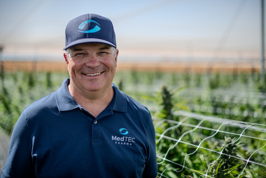 Brad, a fair-skinned middle-aged man, stands smiling amid cannabis plants