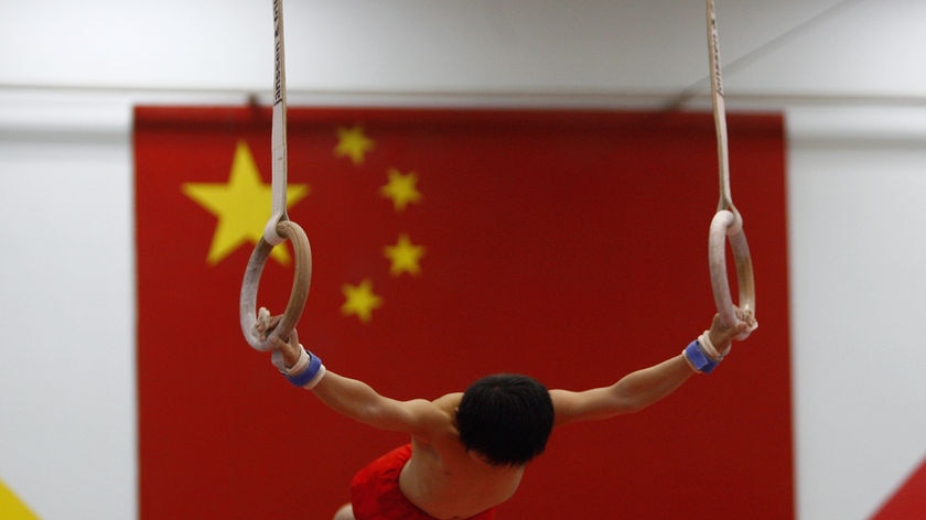 A young Chinese athlete exercises in front of a Chinese flag at a gymnastics hall in Beijing