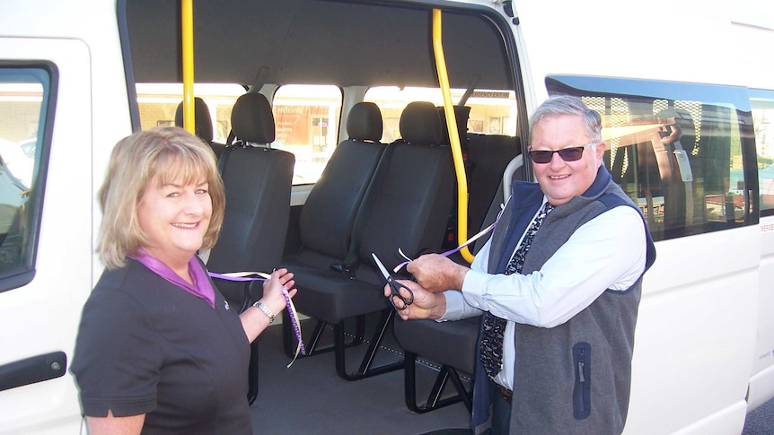 A woman and man cutting a ribbon over the door of a mini bus