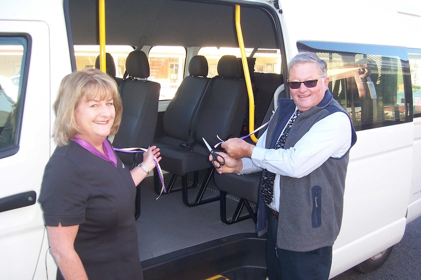 A woman and man cutting a ribbon over the door of a mini bus