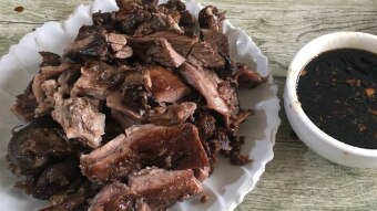 A white plate has cooked meat on it next to a bowl of a dark brown sauce.