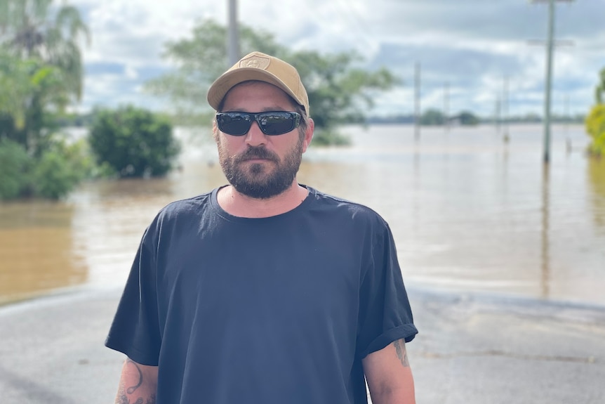 Man in cap and sunglasses stands in front of flood water