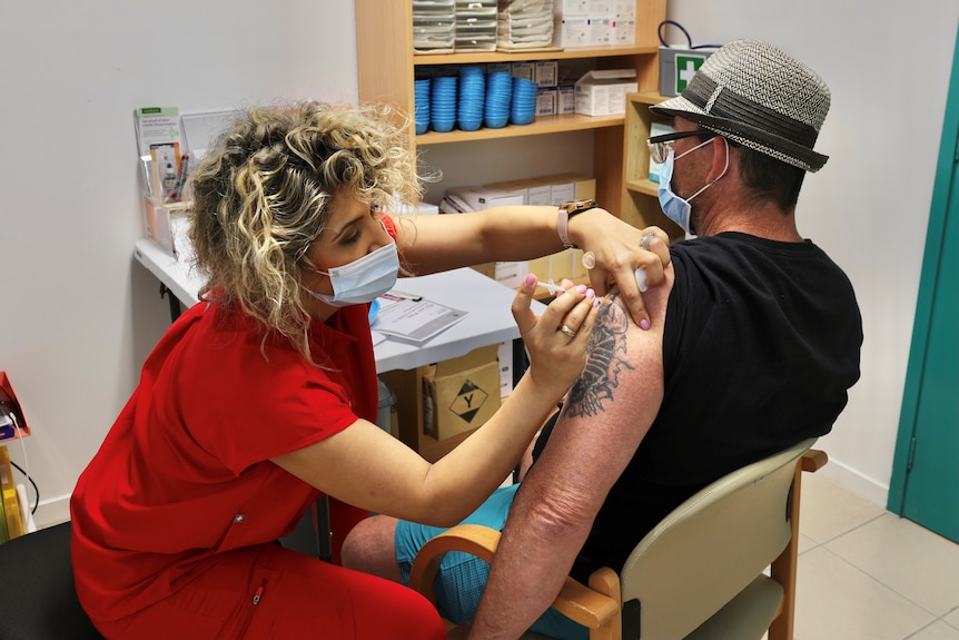 A man recieving a needle to his left arm by a female doctor.