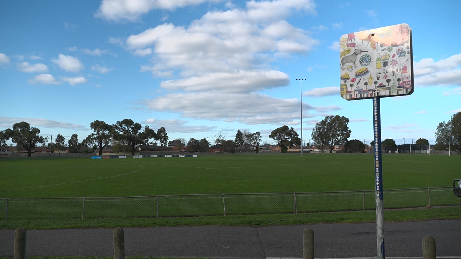 A green oval with white markings for aussie rules football on a partly cloudy day.