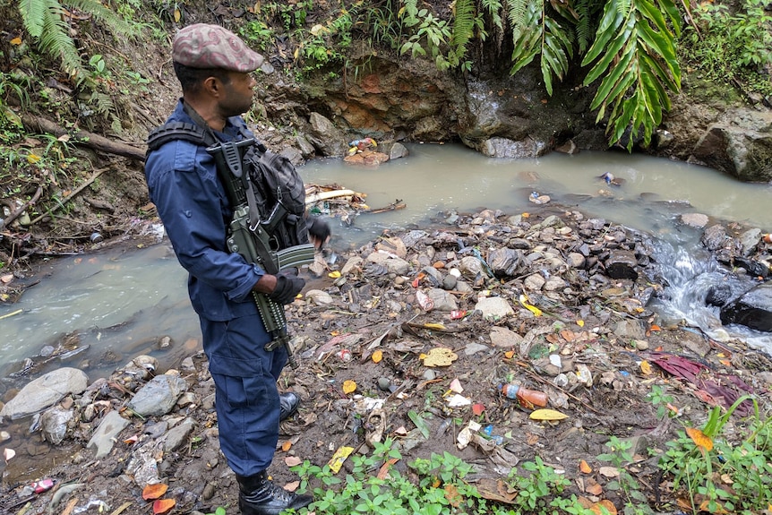 A PNG Policeman holding a gun stands by a creek in the jungle