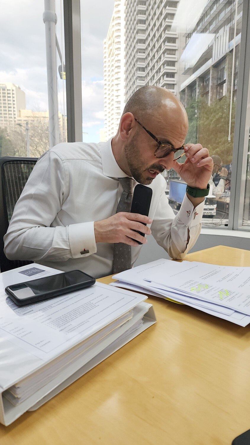 A man wearing glasses talks on his mobile phone while sitting at a desk