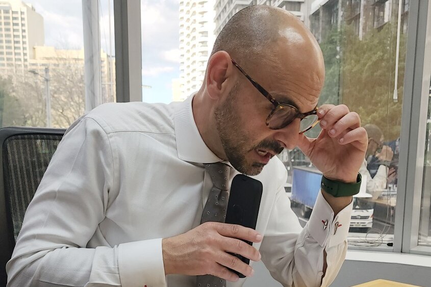 A man wearing glasses talks on his mobile phone while sitting at a desk