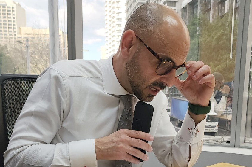 A man wearing glasses talks on his mobile phone while sitting at a desk