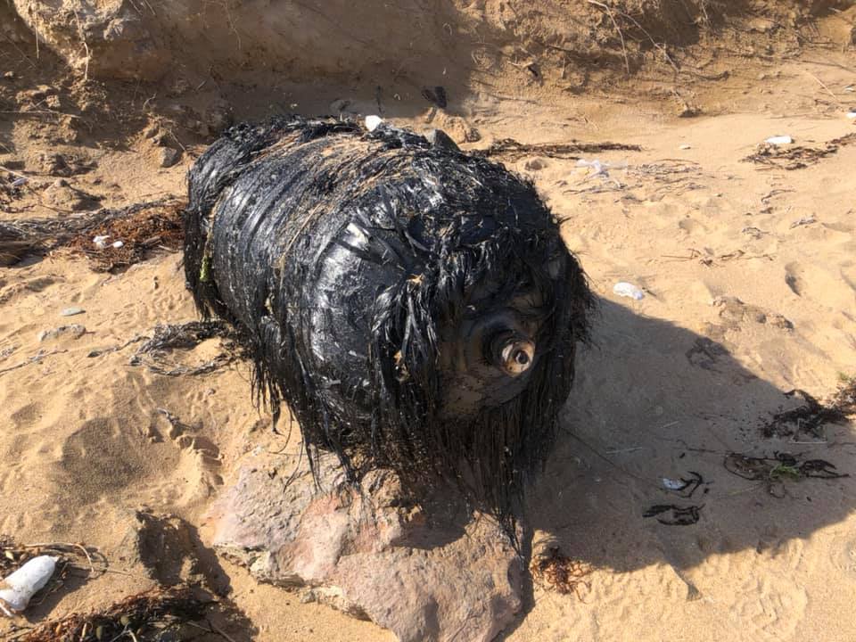 A large black cylinder wrapped in shredded material on sand