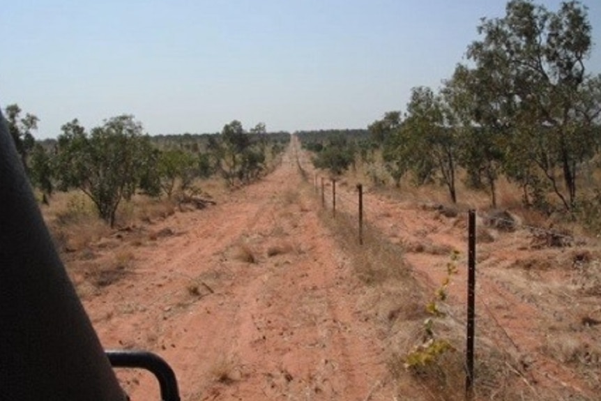 The view through a car windscreen of a dusty dirt outback road alongside a barbed wire fence
