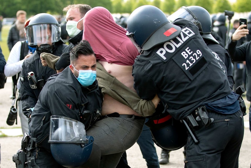 a man with a shirt over his head is arrested by police in riot gear and masks