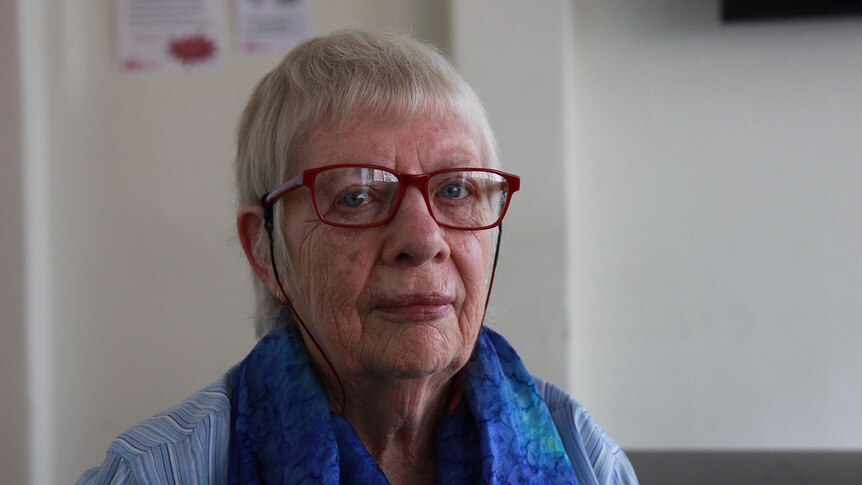 Beryl Noonan looks at the camera from behind red-framed glasses.