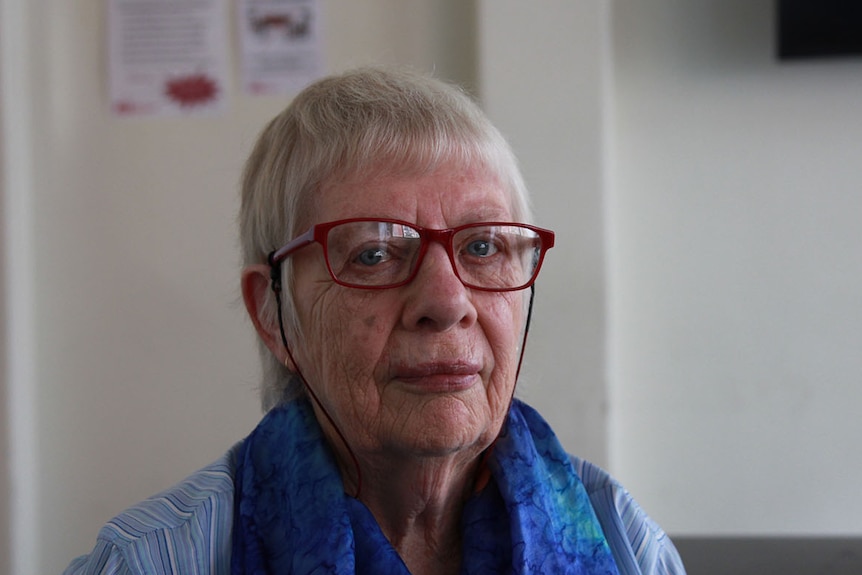 Beryl Noonan looks at the camera from behind red-framed glasses.
