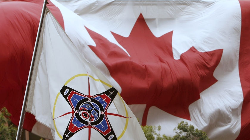 A native flag and a large Canadian flag fly in the wind.