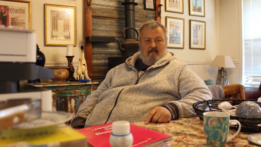 A man sits at a table wearing a grey jumper 
