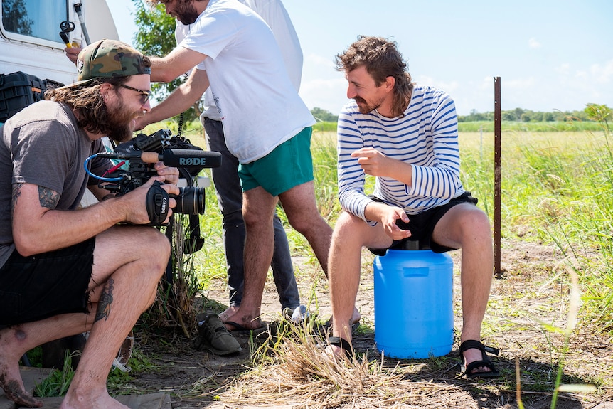 Two men, one holding a camera, sit and talk.