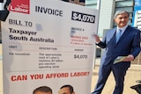 Rob Lucas stands next to a large prop invoice