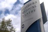 A sign reading Flinders Medical Centre Main Entrance, with a blue cloudy sky and a tree in the background